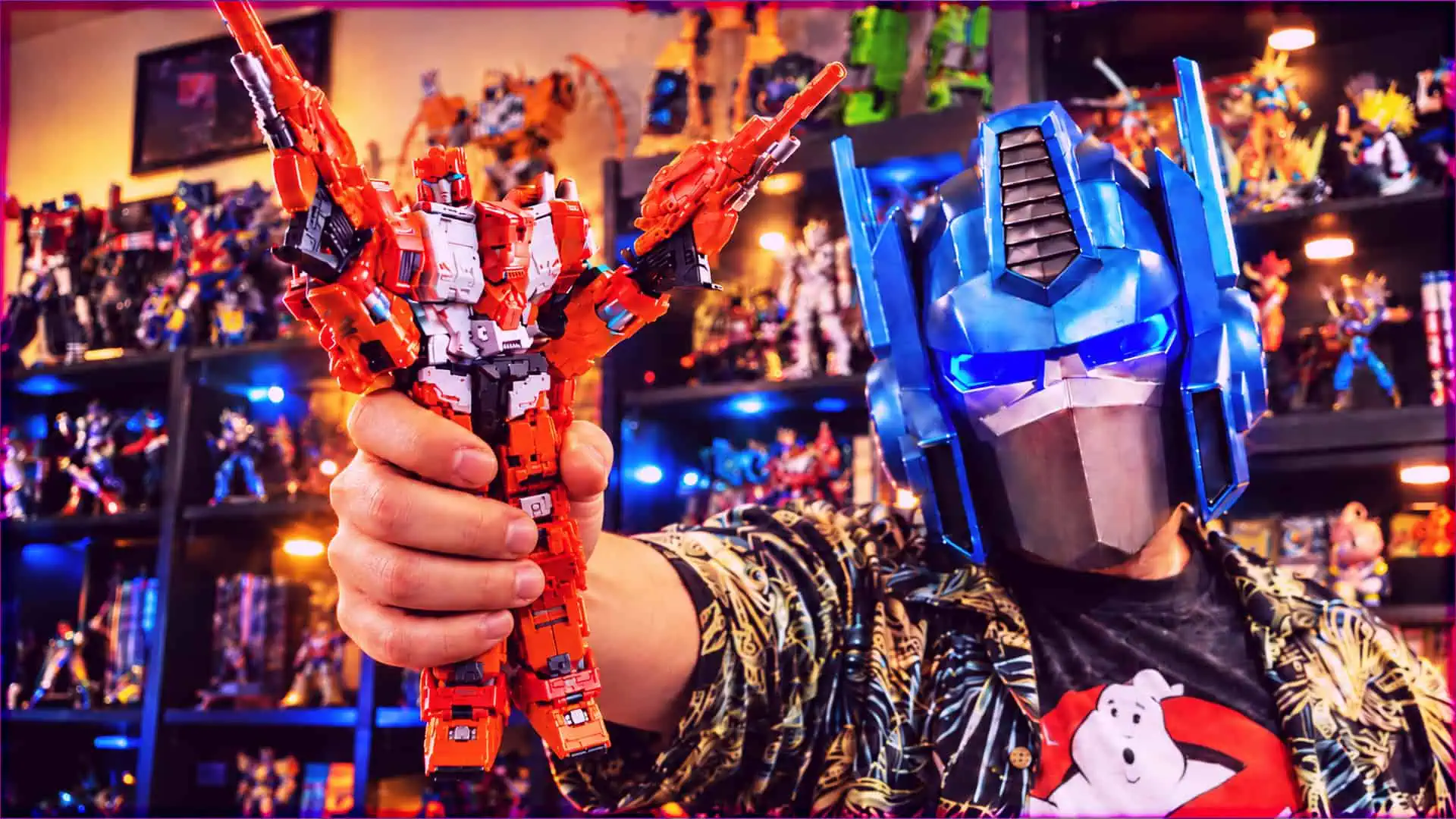Person holding a red and white Transformer toy with a blue robot mask in the background.