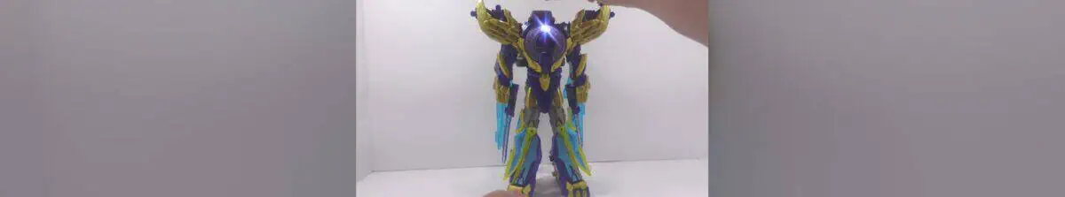 Hand holding a detailed Bruticus Transformer toy with a vibrant pink background.