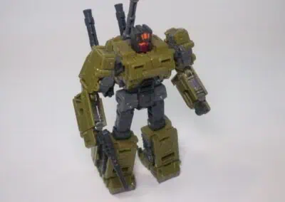 Green and black robot toy with weapons and armor, on white background.